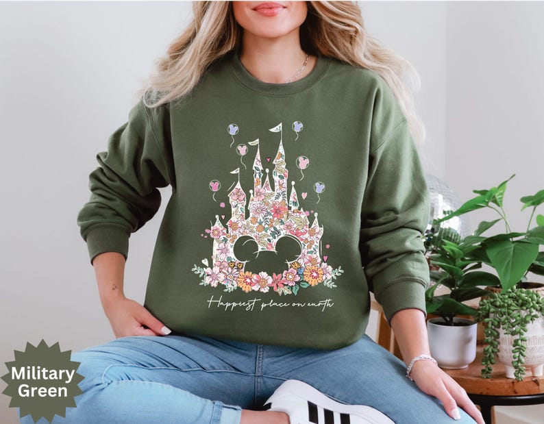 May include: A green sweatshirt with a floral print of a castle and the text "Happiest place on earth".