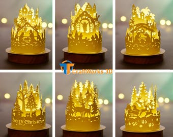 May include: A collection of illuminated paper cutouts depicting Christmas scenes. Each cutout is a different design, including a nativity scene, a forest with deer, and a castle with the text "Merry Christmas". The cutouts sit on wooden bases.