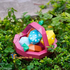 K&ouml;nnte beinhalten: Ein rosa Papierkorb gef&uuml;llt mit geometrischen Papierformen in Blau, Gelb und Orange. Die blaue Form hat wei&szlig;e Herz- und Punktmuster. Der Korb ist von gr&uuml;nem Laub umgeben. Der Text "TCraftWorks 3D" ist sichtbar.