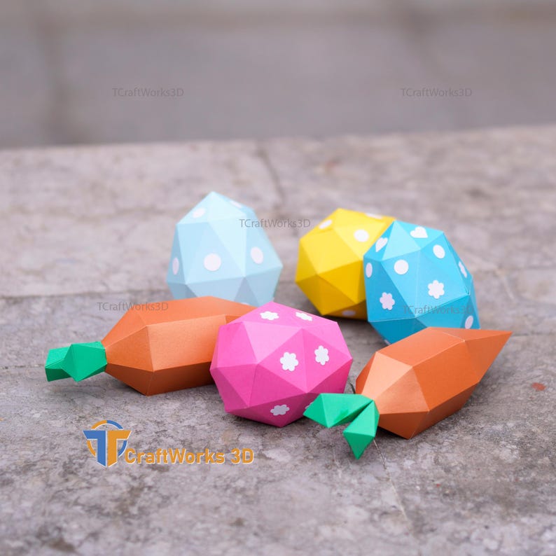 K&ouml;nnte beinhalten: Eine Sammlung farbenfroher, geometrischer Papier-Gem&uuml;se- und Ostereiformen. Die orangefarbenen Karotten haben gr&uuml;ne Spitzen, und die Eier sind blau, gelb und rosa mit wei&szlig;en Tupfen und Blumenakzenten. Der Text "TCraftWorks3D" ist sichtbar.