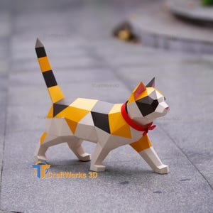 May include: A low-poly geometric cat sculpture featuring a calico pattern of white, orange, and black triangular facets. The cat has a long, upright tail, a red collar around its neck, and pink inner ears, standing in a walking pose on four legs.