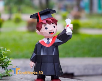 May include: A papercraft graduation figure in a black cap and gown, holding a diploma. The figure has red hair, a red tassel, and a red and white stole. The figure is standing on a stone surface with a blurred green background.