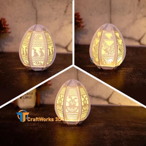 Könnte beinhalten: Drei weiße Papier-Ostereierlampen mit filigranen Ausschnitten. Die Designs beinhalten Hasen, Schmetterlinge und geometrische Muster. Die Lampen werden von innen beleuchtet und erzeugen ein warmes Leuchten.