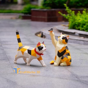 Può includere: Due statuette di gatto geometriche low-poly con un motivo calico di sfaccettature triangolari bianche, arancioni e nere. Un gatto è in piedi con un collare rosso, l'altro è seduto verso una farfalla. Il testo riporta CraftWorks3D.