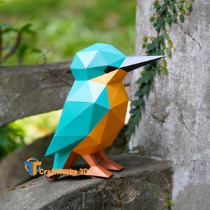 Puede incluir: Escultura geométrica de papel de un martín pescador en turquesa, naranja y marrón. El ave tiene un pico negro y está sobre una superficie de piedra. El texto "CraftWorks 3D" es visible. Una pieza de decoración única.