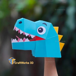 May include: A blue papercraft dinosaur head with white teeth, a red mouth, and a large white and black eye. Yellow triangles form the spines on the back of the head. The logo "TCraftWorks3D" is visible.