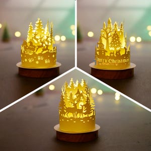 Könnte beinhalten: Drei beleuchtete Weihnachtspapierausschnitte. Jedes hat ein anderes Design: einen Rentierschlitten, ein Schloss mit einem Weihnachtsbaum und Hirsche in einem Wald. Die Ausschnitte stehen auf Holzsockeln, mit den Worten "Ho Ho Ho" und "Merry Christmas" sichtbar.