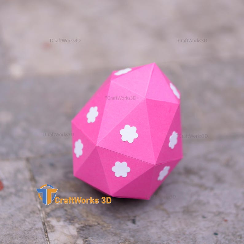 K&ouml;nnte beinhalten: Ein leuchtend rosa, geometrisches Papierobjekt mit wei&szlig;en Blumenakzenten. Die facettenreiche Form deutet auf einen Dekorationsartikel oder einen Teil eines gr&ouml;&szlig;eren Designs hin. Der Text "TCraftWorks3D" ist sichtbar. Ein kreatives Papierdesign.