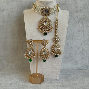 Könnte beinhalten: Ein aufwendiges, goldfarbenes Schmuckset mit Halskette, Anhänger, Ohrringen und Kopfschmuck. Die Halskette und der Anhänger haben klare Steinakzente und sind mit Kunstperlen verziert. Die Ohrringe und der Kopfschmuck haben ebenfalls klare Steinakzente und grüne Perlen.