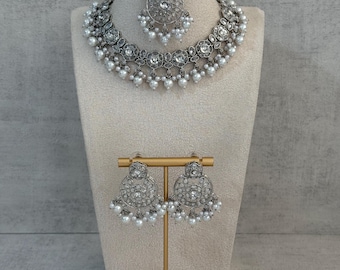 Könnte beinhalten: Ein silberfarbenes Brautschmuck-Set, bestehend aus Halskette, Kopfschmuck und Ohrringen, präsentiert auf einer Schaufensterpuppe. Halskette und Ohrringe weisen ein florales Design mit klaren Steinen und hängenden weißen Perlen auf. Der Kopfschmuck hat ein ähnliches Design.