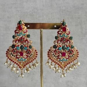 Puede incluir: Pendientes dorados ornamentados con forma de lágrima. Los pendientes presentan piedras preciosas rojas, verdes y turquesas, con pequeñas perlas blancas colgando de la parte inferior. El diseño es intrincado y detallado, con estética vintage.