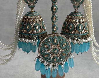 May include: An ornate, antique-style jewelry set featuring turquoise and gold accents. The set includes large bell-shaped earrings, a headpiece, and a pendant, all adorned with small stones and dangling blue beads. White pearl strands are also included.