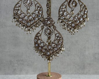 May include: An antique gold-toned jewellery set, including earrings and a headpiece, displayed on a wooden stand. The earrings and headpiece feature clear, sparkling stones and small, dangling pearls. The set is ornate and elegant.