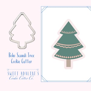May include: A silver metal Boho Scandi Tree cookie cutter next to a green and pink illustration of a Christmas tree. The illustration has a light pink background and a blue border. Text on the image reads "Boho Scandi Tree Cookie Cutter" and "Sweet Adaline's Cookie Cutter Co."