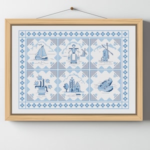 Puede incluir: Una obra de arte en punto de cruz enmarcada con diseños holandeses en azul y blanco. La obra de arte incluye imágenes de un velero, un molino de viento y figuras holandesas tradicionales. El marco es de madera clara y está colgado en una pared blanca.