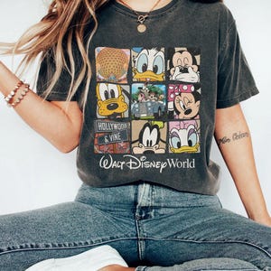 Op de afbeelding: Een grijs T-shirt met een vintage-stijl grafische afbeelding van verschillende Disney-figuren en de tekst "Walt Disney World" en "Hollywood & Vine".