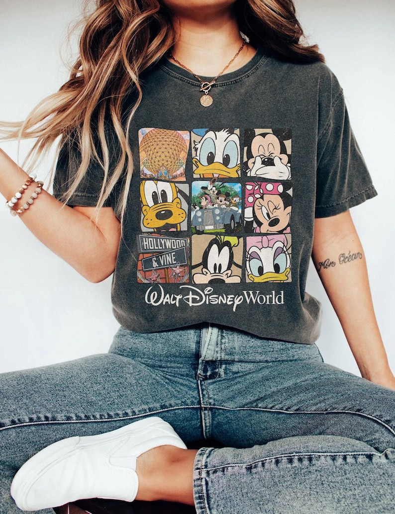 Op de afbeelding: Een grijs T-shirt met een vintage-stijl grafische afbeelding van verschillende Disney-figuren en de tekst "Walt Disney World" en "Hollywood & Vine".