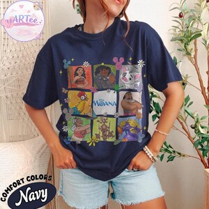 May include: Navy blue t-shirt featuring a grid of Moana characters. The shirt includes images of Moana, Maui, Pua, Hei Hei, and others. The word "Moana" is printed in the center. The shirt also has the words "Comfort Colors Navy" printed on the bottom.