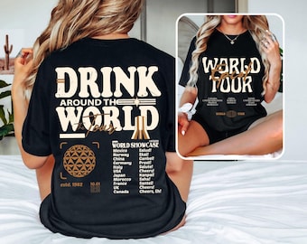 May include: Black t-shirt with a white graphic that says "Drink Around the World Tour" and features a globe, a tower, and a list of countries with their cheers. The graphic also includes the text "World Showcase" and "estd. 1982 10.01".