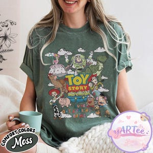 May include: Green t-shirt featuring a colorful graphic of characters from the animated film "Toy Story." The design includes Buzz Lightyear, Woody, and other beloved characters, with the text "TOY STORY" and "YOU'VE GOT A FRIEND IN ME."