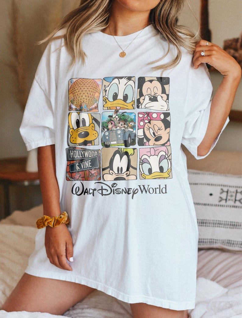 Op de afbeelding: Wit overformaat T-shirt met een grafische print van verschillende Disney-figuren, waaronder Mickey Mouse, Minnie Mouse, Donald Duck, Goofy en Pluto. Het shirt heeft ook de tekst "Walt Disney World" en "Hollywood & Vine".