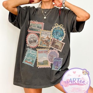 以下が含まれることがあります： ヴィンテージスタイルの切手のコラージュが特徴の濃いグレーのTシャツ。切手は海賊船や未来的な乗り物など、さまざまなアトラクションを描いています。ゆったりとしたフィット感で、色あせたヴィンテージ感があります。