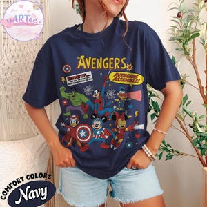 May include: Navy blue t-shirt featuring a graphic of The Avengers characters, including Hulk, Spider-Man, and Mickey Mouse. The shirt has the text "The Avengers" and "Avengers Assemble!" printed on it. The shirt is labeled "Comfort Colors Navy".