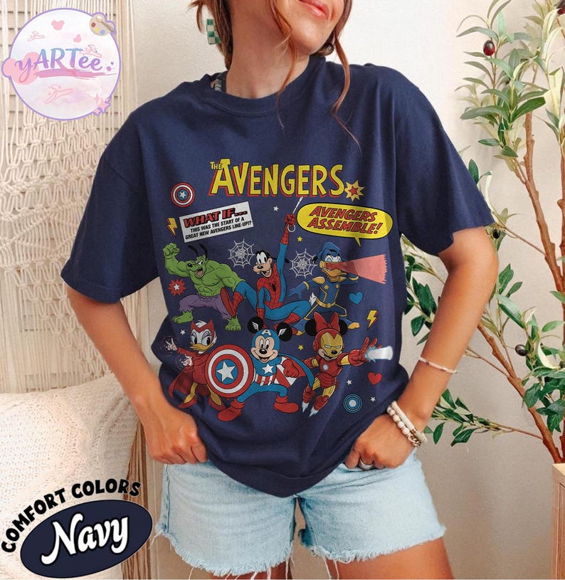 May include: Navy blue t-shirt featuring a graphic of The Avengers characters, including Hulk, Spider-Man, and Mickey Mouse. The shirt has the text "The Avengers" and "Avengers Assemble!" printed on it. The shirt is labeled "Comfort Colors Navy".