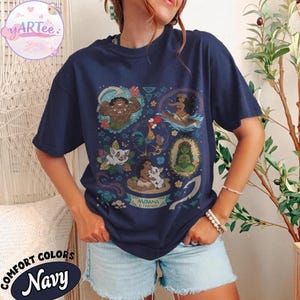 K&ouml;nnte beinhalten: Marineblaues T-Shirt mit einem farbenfrohen Aufdruck von Figuren aus dem Animationsfilm Moana. Das Design enth&auml;lt Bilder von Maui, Moana, Pua, Hei Hei und anderen Elementen. Der Text "Moana & Friends" ist ebenfalls sichtbar.