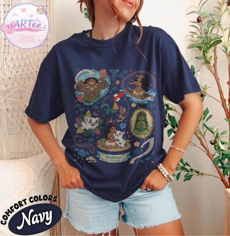 K&ouml;nnte beinhalten: Marineblaues T-Shirt mit einem farbenfrohen Aufdruck von Figuren aus dem Animationsfilm Moana. Das Design enth&auml;lt Bilder von Maui, Moana, Pua, Hei Hei und anderen Elementen. Der Text "Moana & Friends" ist ebenfalls sichtbar.