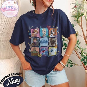 May include: Navy blue t-shirt featuring a colorful graphic of characters from the Disney movie "Frozen." The design includes images of Anna, Elsa, Olaf, Kristoff, Sven, and other characters. The shirt also has the text "Frozen" in the center.