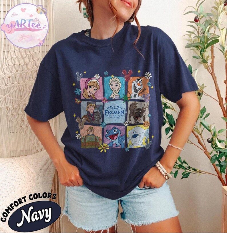 May include: Navy blue t-shirt featuring a colorful graphic of characters from the Disney movie "Frozen." The design includes images of Anna, Elsa, Olaf, Kristoff, Sven, and other characters. The shirt also has the text "Frozen" in the center.