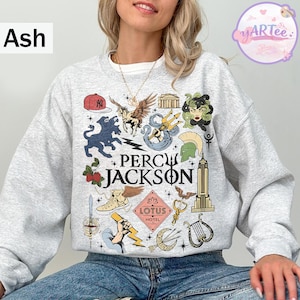 Pu&ograve; includere: Felpa grigia cenere con un design grafico colorato con la scritta "Percy Jackson". Il design include illustrazioni di creature mitologiche, un berretto da baseball e l'Empire State Building. Girocollo.