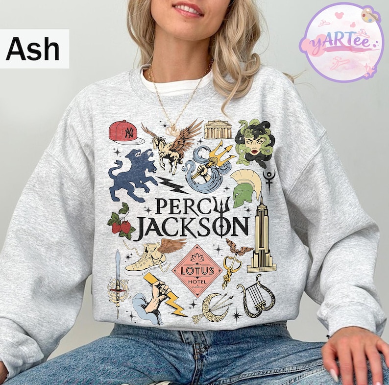 Pu&ograve; includere: Felpa grigia cenere con un design grafico colorato con la scritta "Percy Jackson". Il design include illustrazioni di creature mitologiche, un berretto da baseball e l'Empire State Building. Girocollo.