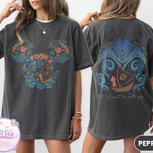 May include: Dark gray t-shirt with a colorful graphic on the front and back. The front features a Mickey Mouse-shaped design with floral and boat motifs, and text. The back has a boat design and text. The shirt is a casual wear item.