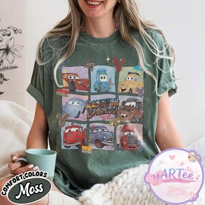 May include: Green t-shirt featuring a grid of cartoon cars from the movie Cars. The shirt has the text "Radiator Springs" and "Lightning McQueen". The shirt also has the text "Comfort Colors Moss" on the bottom left.