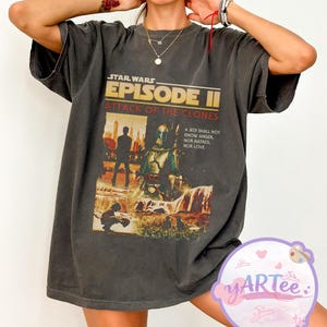 May include: Dark gray t-shirt featuring a Star Wars Episode II: Attack of the Clones graphic. The design includes characters and text: "A Jedi shall not know anger, nor hatred, nor love." The shirt has a vintage, worn look.