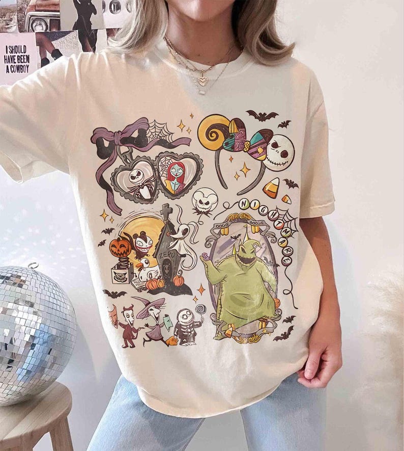 May include: Cream-colored t-shirt featuring a colorful graphic design with characters and elements from "The Nightmare Before Christmas." The design includes Jack Skellington, Sally, Oogie Boogie, and other iconic imagery. The shirt has short sleeves and a crew neck.