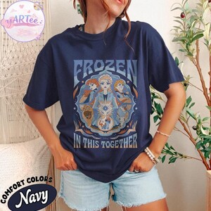 May include: Navy blue t-shirt featuring the text "FROZEN IN THIS TOGETHER" and a graphic of characters from the film Frozen. The shirt has a round neck and short sleeves. The shirt is made of Comfort Colors material.