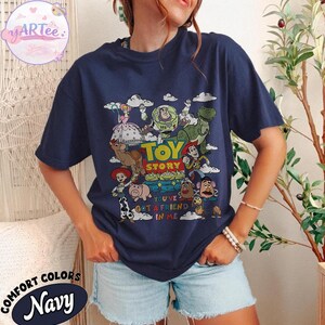 May include: Navy blue t-shirt featuring a colorful graphic of Toy Story characters, including Woody, Buzz Lightyear, and Rex. The text "TOY STORY" and "YOU'VE GOT A FRIEND IN ME" are also displayed. The shirt is labeled "COMFORT COLORS Navy".