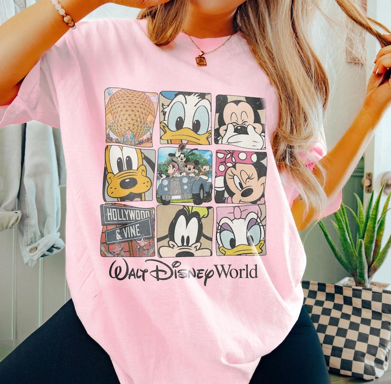 Op de afbeelding: Roze T-shirt met een grafische print van verschillende Disney-figuren, waaronder Mickey Mouse, Donald Duck, Goofy en Pluto. Het shirt heeft ook de tekst "Walt Disney World" en "Hollywood & Vine".