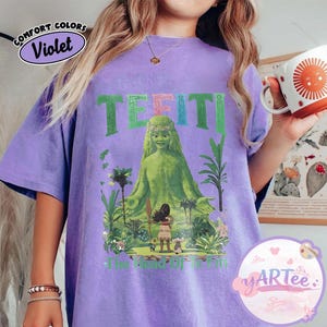 K&ouml;nnte beinhalten: Violettes Comfort Colors T-Shirt mit einem Aufdruck von Te Fiti aus Moana. Das Design enth&auml;lt das Wort "TE FITI" in Gr&uuml;n und Rosa, mit einem Bild von Te Fiti, umgeben von tropischen Pflanzen und dem Text "The Heart of Te Fiti".