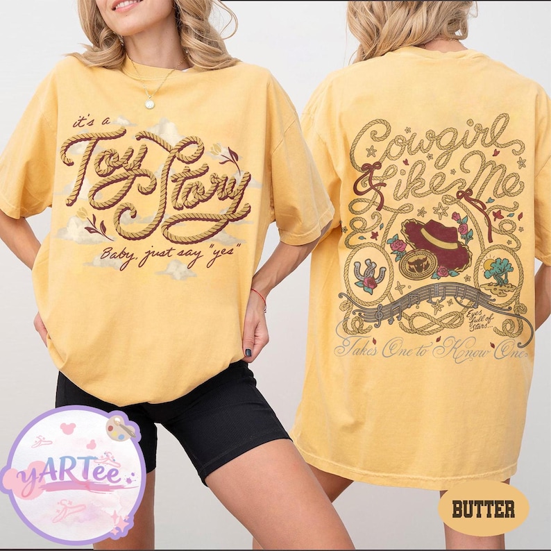May include: A yellow t-shirt featuring a front graphic with rope-style text reading "it's a Toy Story Baby, just say yes" and a back graphic with "Cowgirl & like Me" text, a cowboy hat, roses, a horseshoe, and a desert landscape illustration.