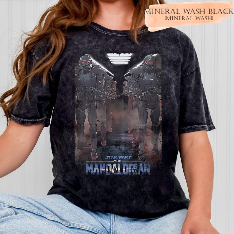 May include: Black mineral wash t-shirt featuring a graphic from Star Wars: The Mandalorian. The design shows two figures in dark armor with red visors, holding weapons. The text "STAR WARS THE MANDALORIAN" is displayed in blue.