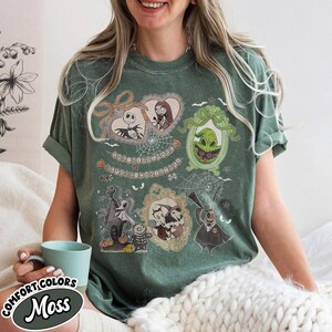 Puede incluir: Camiseta verde musgo con ilustraciones enmarcadas de personajes de The Nightmare Before Christmas. La camiseta incluye a Jack Skellington, Sally, Oogie Boogie y otros personajes. El texto "The Nightmare Before Christmas" tambi&eacute;n es visible.
