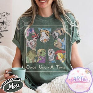 May include: Moss green t-shirt featuring a graphic of cartoon characters from various animated films. The graphic is framed with a white border and includes the text "Once Upon A Time". The shirt is made of a soft, comfortable material.