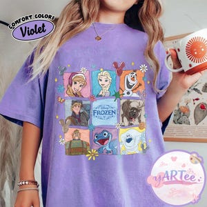 May include: Violet-colored t-shirt featuring a grid of Disney Frozen characters. The design includes Anna, Elsa, Olaf, Kristoff, Sven, and other characters. The shirt has the text "Disney Frozen" and "Comfort Colors" in a circular design.