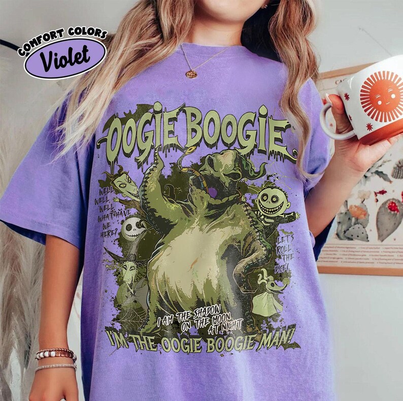Puede incluir: Una camiseta de color violeta con un gr&aacute;fico del personaje Oogie Boogie de The Nightmare Before Christmas. El dise&ntilde;o incluye el texto "Oogie Boogie" y otras frases. La camiseta es de la marca Comfort Colors.