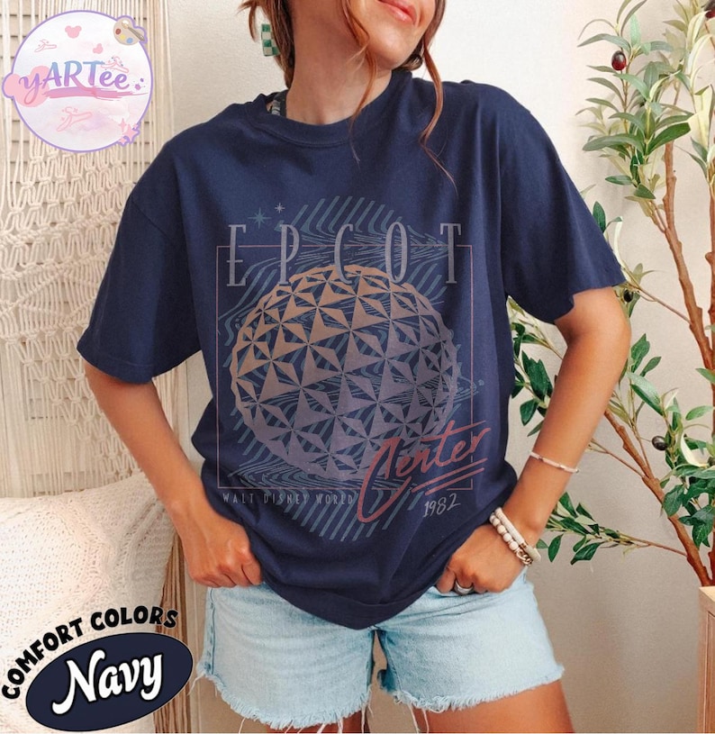 May include: Navy blue t-shirt with a graphic of the EPCOT Center ball, the word "EPCOT" above it, and "Winter 1982" below. The shirt is labeled "Comfort Colors Navy".