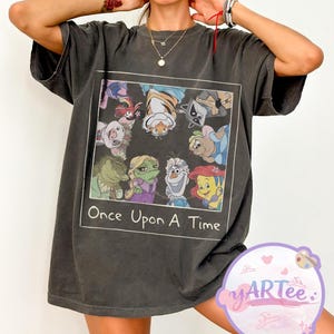 May include: Dark gray t-shirt featuring a rectangular graphic with cartoon characters and the text "Once Upon A Time." The graphic includes a variety of animated figures. The shirt has short sleeves and a relaxed fit.